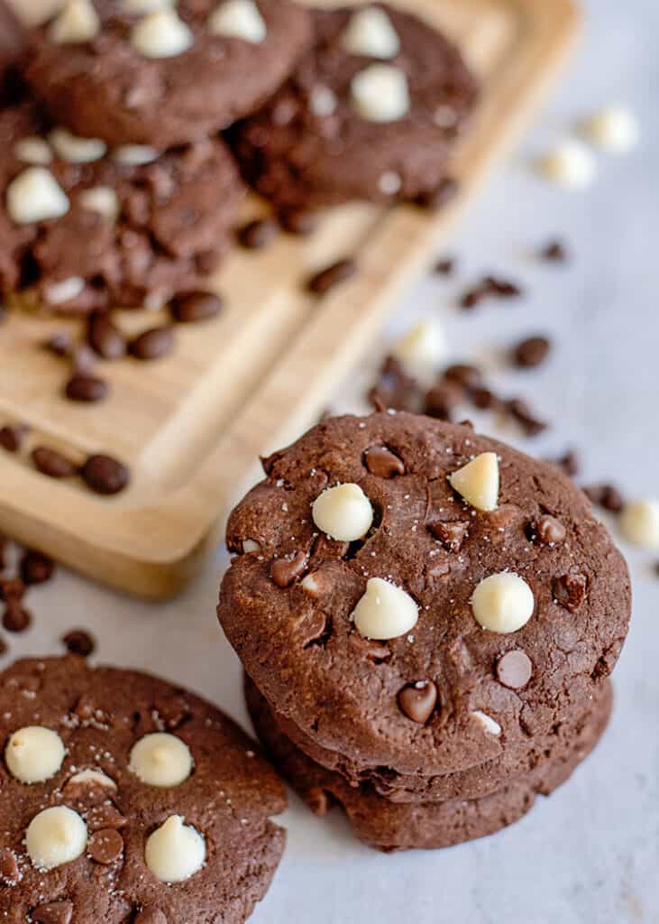 stack of cookies on a marble surface with chocolate chips around it and a cutting board